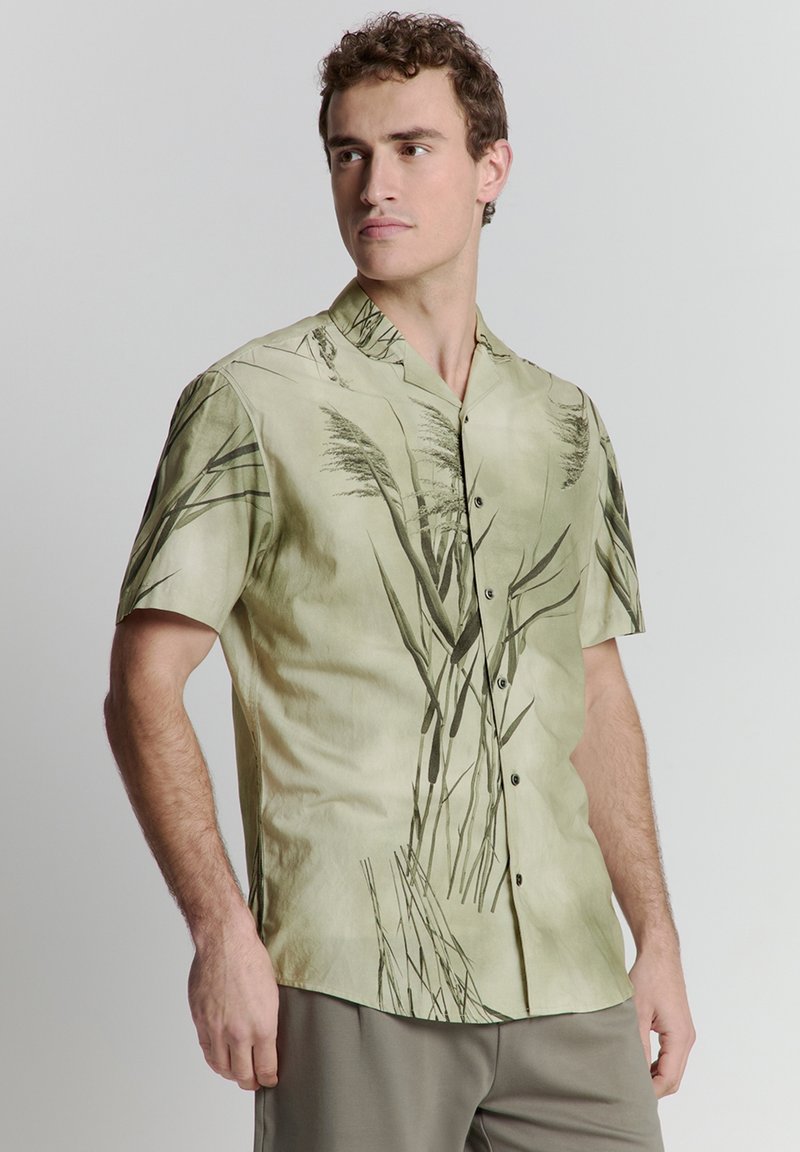 Korte mouw shirt in lichtgroen met een donkergroen plantenpatroon, gemaakt van een gladde stof. Heeft een notch-kraag en knopen aan de voorkant.