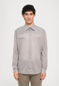 Pruhovaná košile na knoflíky ve světlé šedé a bílé barvě, s dlouhými rukávy, špičatým límcem a dvěma náprsními kapsami s knoflíkovými akcenty.
