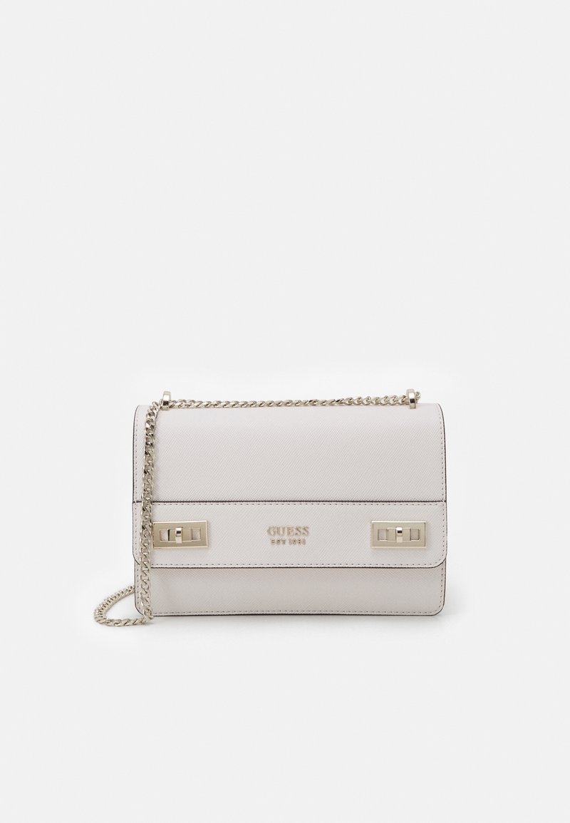 White leather crossbody bag with a gold chain strap, gold turn-lock closures, and "GUESS EST 1981" embossed on the front.