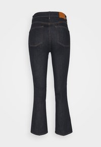 Jean en denim bleu foncé avec une jambe légèrement évasée, poches arrière visibles, coutures jaunes et une écusson en cuir marron sur la ceinture.