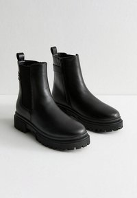 Botas negras de cuero hasta el tobillo con una suela de goma gruesa, paneles laterales elásticos, tiradores y un zipper lateral para facilitar su uso.