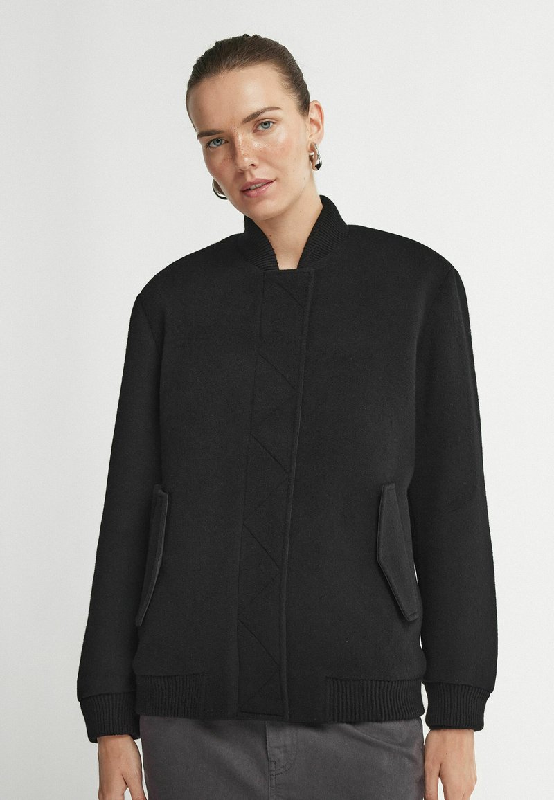 Svart bomberjacka i texturerad kvalitet. Ribbat manschetter och krage. Sidofickor med snedställda öppningar. Har ett centralt diamantmönster.