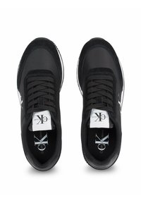 Baskets de sport noires avec une tige en textile lisse, des accents en suède, des lacets ronds et un logo blanc sur la languette et le côté.