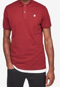 Burgunderröd polo skjorta i bomullstyg, med en tvåknappsslutning, korta ärmar och en liten logga på bröstet.