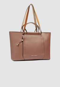 Bruine leren shopper met lange handvatten; heeft een voorvak met een subtiele trekband en een metalen logodetail. Gladde textuur.