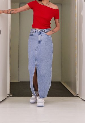 Röd off-shoulder topp kombinerad med en ljusblå denim maxikjol med en framficka. Modellen bär vita sneakers som visar en avslappnad stil.