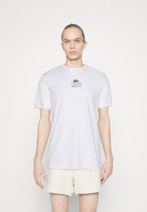 Hvid bomuld t-shirt med korte ærmer, har et grønt broderet logo og tekst på fronten, rund halsudskæring og en afslappet pasform.