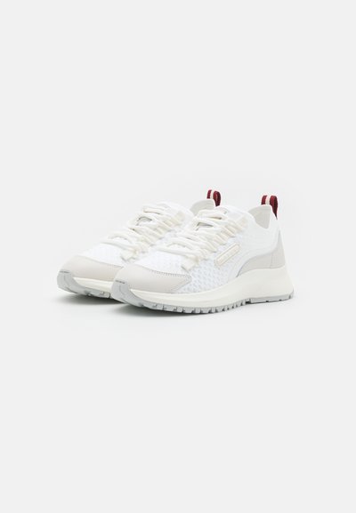 White athletic sneakers with mesh upper, gray accents, and red pull tabs. Features textured design, contrasting sole, and traditional lacing.