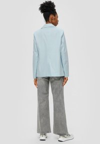 Blazer azzurro chiaro con vestibilità su misura, ampie alette e apertura posteriore singola, abbinato a jeans grigi a gamba ampia e sneakers casual.