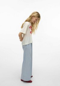 Hvit t-skjorte med rød grafisk tekst, kombinert med lyseblå stripete vide bukser. Brukt med røde sko, med en avslappet passform og myk tekstur.