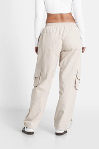 Beige cargobroek met een ontspannen pasvorm, elastische tailleband, zijvakjes en een trekkoord aan de onderkant. Lichte stof met een soepele textuur.