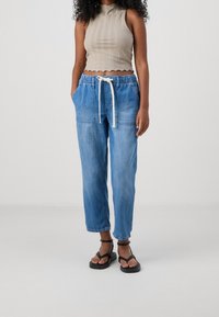 Jasnoniebieskie dżinsowe joggery z elastycznym pasem i sznurkiem, z dwiema przednimi kieszeniami. Połączone z beżowym prążkowanym topem w stylu crop i czarnymi sandałami.