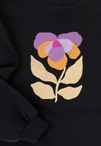 Zwarte hoodie met een grote geborduurde bloem in paarse en oranje tinten, vergezeld van beige bladeren, die textuur en gedetailleerde stiksels laat zien.