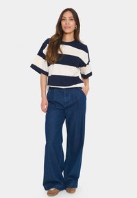 Striped t-shirt in navy and cream, with a relaxed fit and short sleeves. Paired with wide-leg blue denim pants and brown footwear.