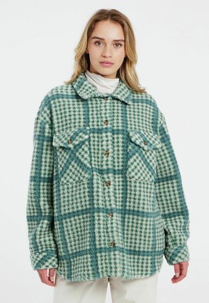 Groene en crèmekleurige geruite shacket van zacht, fuzzy materiaal, met een kraag, twee borstzakken en een knoopsluiting aan de voorkant.