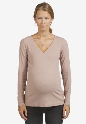 Long-sleeve, light pink maternity top with a wrap design, ribbed texture, and a scalloped neckline detailing, worn over dark pants.