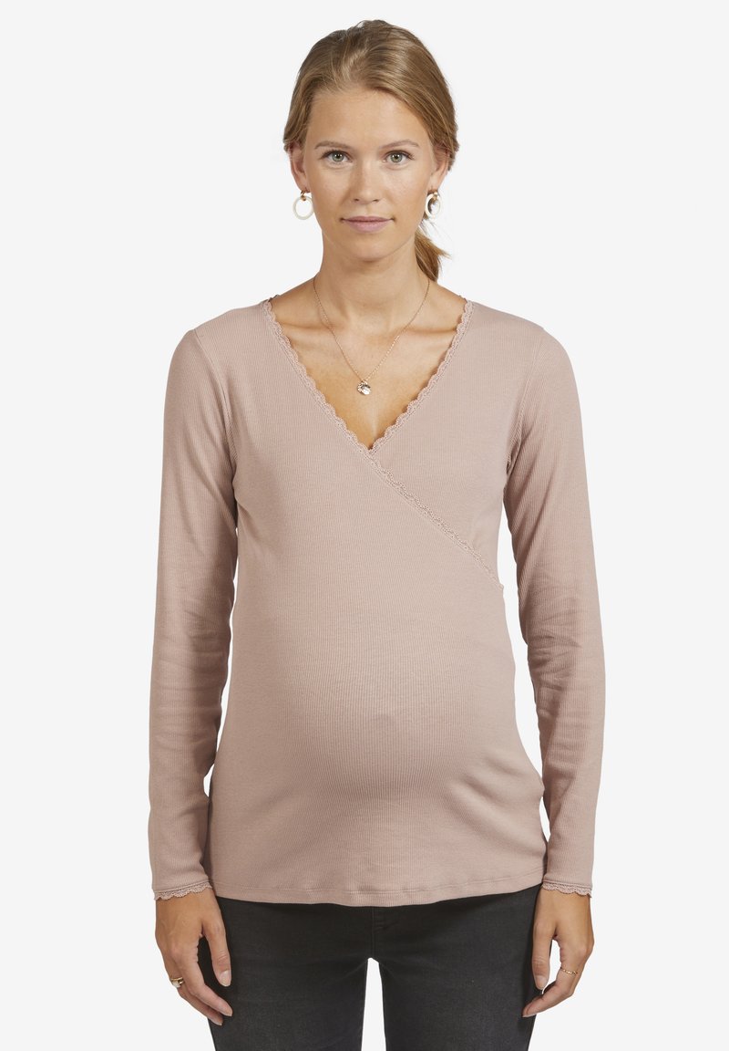 Langärmliges, hellrosa Stilloberteil mit Wickeldesign, gerippter Textur und gewelltem Ausschnitt, getragen über dunklen Hosen.