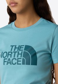 Lysblå bomulds T-shirt med et mørkeblå logo print af "THE NORTH FACE" og en halvmåne grafik på forsiden. Rund halsudskæring, korte ærmer.