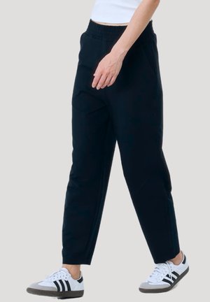 Black jogger pants with an elastic waistband, side pockets, and tapered legs, paired with white sneakers featuring black stripes.
