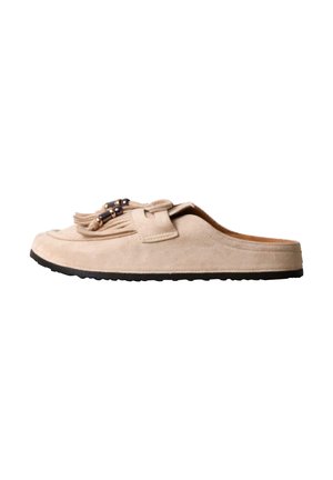 Mocassin beige en daim sans talon avec semelle noire, pampilles et perles décoratives sur le dessus.
