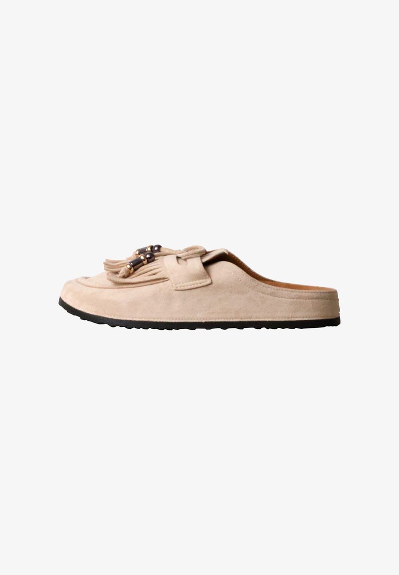 Mocassin beige en daim sans talon avec semelle noire, pampilles et perles décoratives sur le dessus.