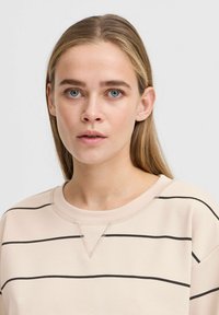 Sweatshirt rose clair avec des rayures horizontales noires, un col rond et un détail en V au niveau du col. Texture douce avec une coupe décontractée.