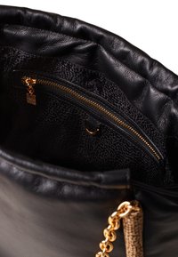 Black leather handbag with a textured interior, featuring a gold zipper pocket and chain accent. Interior has a subtle patterned lining.