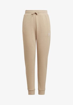 Pantalon de survêtement beige fuselé avec taille élastique, cordon de serrage, poches latérales, chevilles resserrées et petit logo Adidas blanc sur la cuisse gauche.