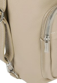 Beige leren handtas met een gestructureerde afwerking, zilveren hardware en zichtbare ritssluiting. Inclusief een zijvak met een merklabel.