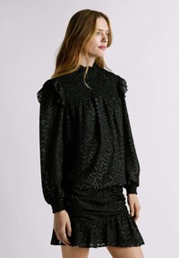 Blusa nera con maniche a volant, tessuto testurizzato e scollatura arricciata. Abbinata a una gonna corta, arricciata, con orlo a frill.