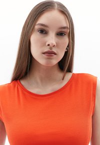 Top senza maniche a coste arancione con scollatura rotonda. Tessuto dalla texture liscia, design aderente, stile minimalista.