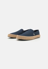 Chaussures slip-on en toile bleu marine avec une semelle en jute tressé, dotées d'un petit logo et de panneaux élastiques sur les côtés pour un enfilage facile.
