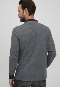 Cămașă polo gri cu mânecă lungă, dintr-un material texturat, cu guler bleu închis și detalii de cusătură contrastantă pe margini.