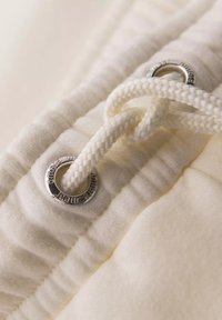 Fermeture à cordon de serrage sur tissu crème avec œillet en métal. Surface texturée avec des plis et un cordon tressé pour l'ajustement.