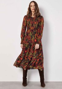 Langes, gestuftes Kleid mit bunten Blumen- und abstrakten Mustern, langen Ärmeln und gerafftem Oberteil. Hergestellt aus leichtem, fließendem Stoff.