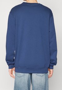 Námořnická modrá mikina, dlouhé rukávy, žebrované manžety a lem, vyrobená z měkké tkaniny. Jednoduchý design bez viditelných log nebo vzorů.