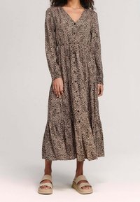 Långärmad klänning med leopardmönster, V-ringning, insvängd midja och lager på lager-skirt. Mjuk tyg med en naturlig beige och brun färgskala.