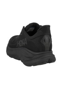 Černá sportovní obuv s texturovaným síťovaným svrškem, polstrovanou podrážkou a logem HOKA. Obsahuje polstrovaný límec a reflexní detaily.