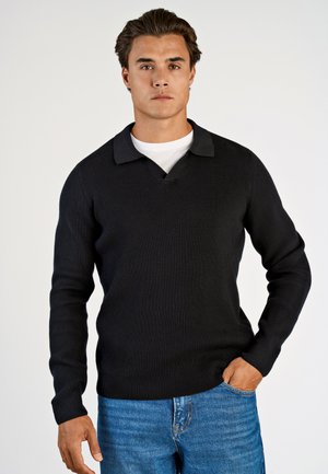 Svart ribbad stickad tröja med V-hals och krage, långa ärmar, tillsammans med blå denimjeans. Ren design, texturerad tyg.