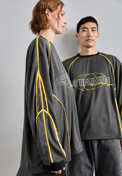 Oversized szare dresy z tkaniny z żółtymi akcentami i logo. Jeden ze stylów ma szerokie rękawy, podczas gdy drugi ma okrągły dekolt.