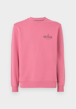 Rosa bomullströja med ribbade manschetter och nederkant, med en liten logotyp i mörk marinblå text på vänster bröstområde. Rund halsringning.