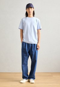 Light blue short-sleeve t-shirt, loose blue denim pants, and white sneakers. Dark blue cap completes the casual outfit.