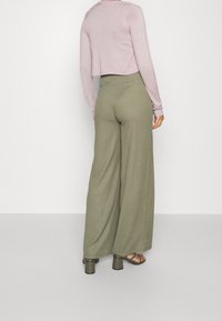 Lichtroze cropped trui gecombineerd met loszittende olijfgroene wijde broek. De broek heeft een hoge taille en een getextureerde stof.