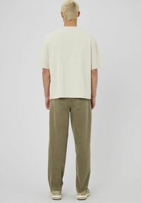 T-shirt en coton surdimensionné de couleur blanc cassé avec des manches courtes, associé à un pantalon olive décontracté avec des poches arrière et une finition texturée.