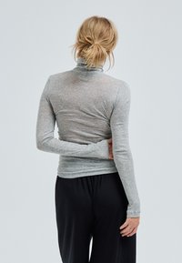Maglietta grigia a maniche lunghe con collo alto, dalla vestibilità slim e tessuto morbido, indossata con pantaloni neri larghi. Vista posteriore mostrata.