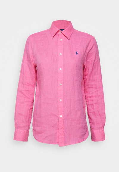 Långärmad, kragad skjorta i ljusrosa linne, med en liten blå logo på vänster bröst och vita knappar framtill.