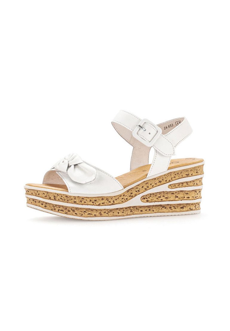 White leather wedge sandal with a bow accent, adjustable ankle strap, and cork-like textured platform featuring cut-out designs.