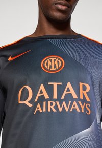 Uomo che indossa una maglietta da calcio nera e arancione dell'Inter Milan con il logo dello sponsor Qatar Airways e il baffo Nike.