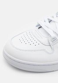 Zapatilla blanca de cuero con caja de dedos perforada, cordones blancos planos y suela de goma texturizada. Presenta costuras grises y sutiles acentos.