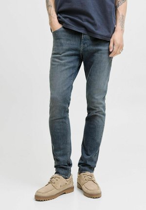 Jeans i blekblå denim med slim fit, försedda med fem fickor och bältesöglor. Kombinerade med beige mockaskor. Slät textur.